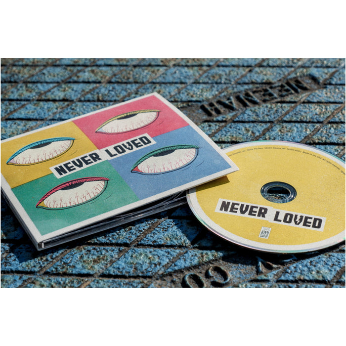 Square CD with NEVER LOVED written in the center in black font over a white background. There are four smaller squares in yellow, red, green, and blue, each with its contrasting color's eyeball drawn inside. To the right of the cover is a yellow disc with NEVER LOVED written in black font in the bottom center