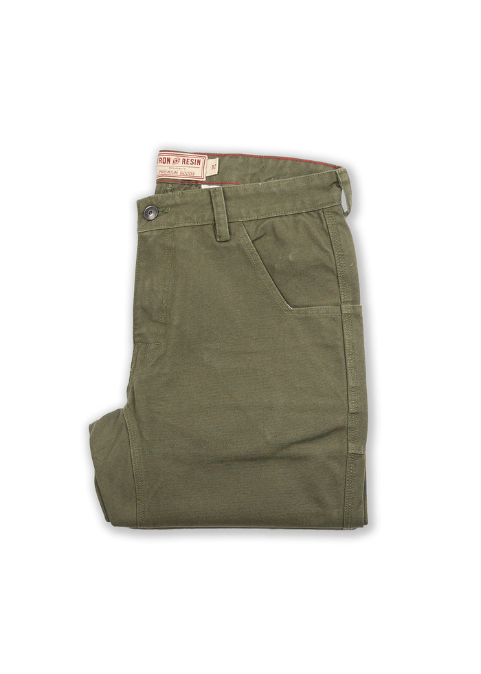 Olive green pants folded neatly, featuring a button closure and side pocket. Visible "Iron & Resin" label on the waistband.