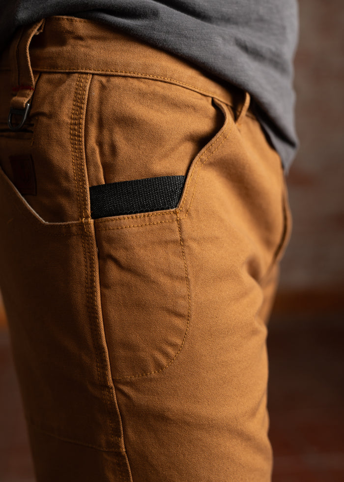 Close-up of a person wearing brown pants with a black pocket detail, paired with a gray shirt, highlighting casual style.