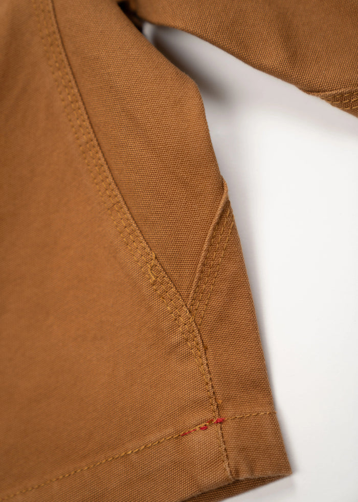 Close-up of brown fabric with detailed stitching and a small red thread accent on a white background.