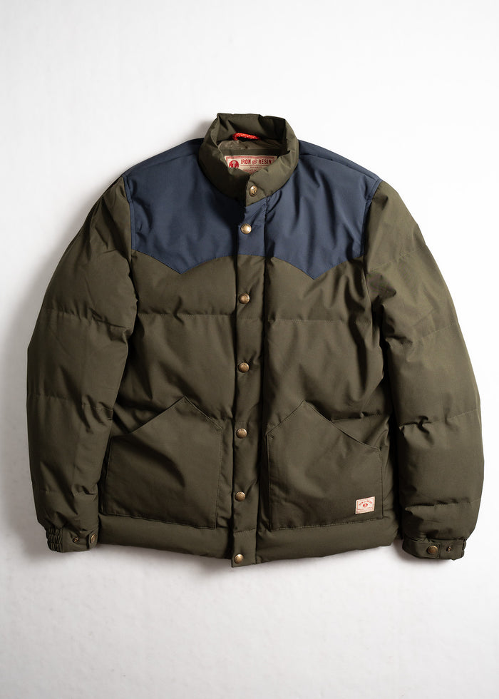 Green and navy puffer jacket with button closure, featuring two front pockets, displayed against a plain white background.