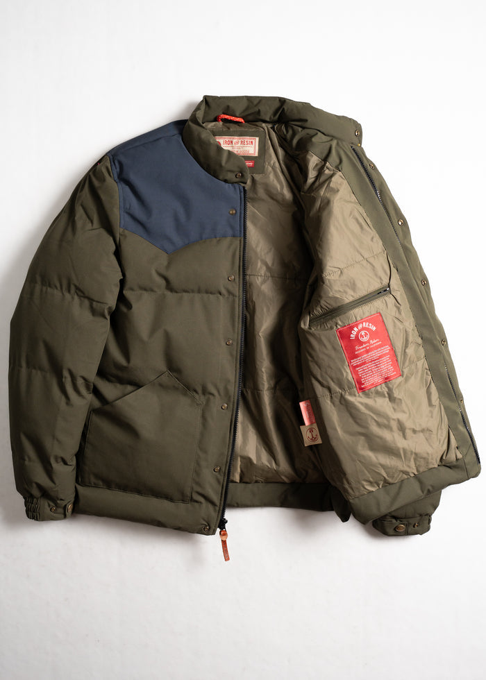 Green puffer jacket with blue shoulder patch, open to reveal beige lining and red label inside. Iron and Resin branding visible.