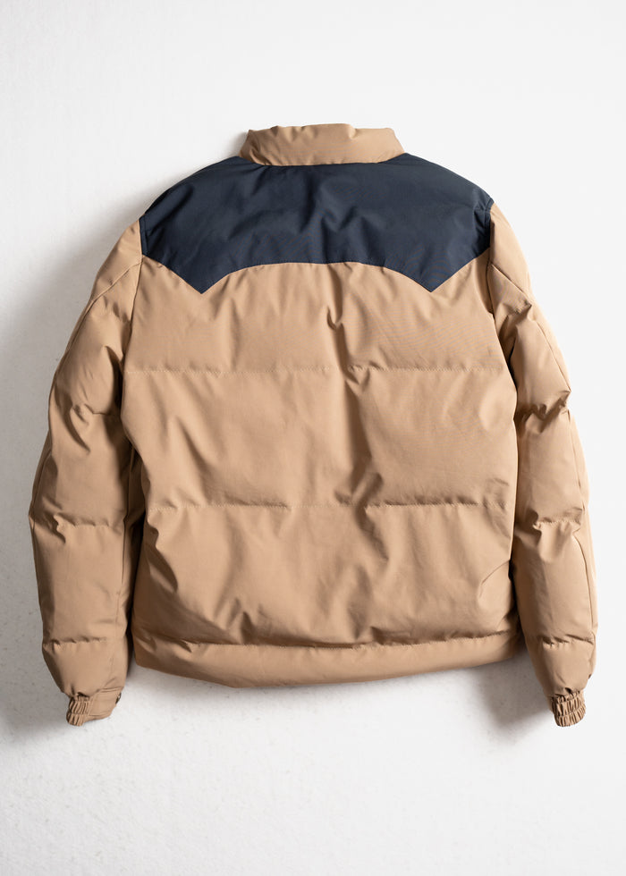 Tan puffer jacket with a navy yoke, displayed against a white background, showcasing its back and quilted design.