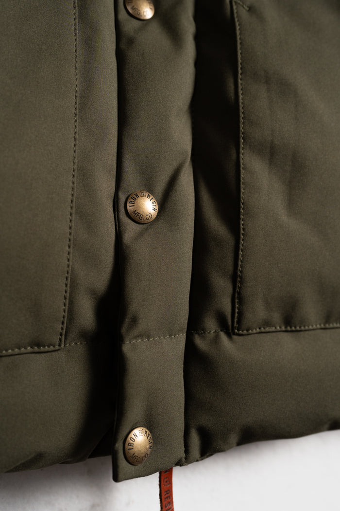 Close-up of an olive green jacket with bronze buttons engraved "Iron and Resin MFG Co," highlighting its rugged design.