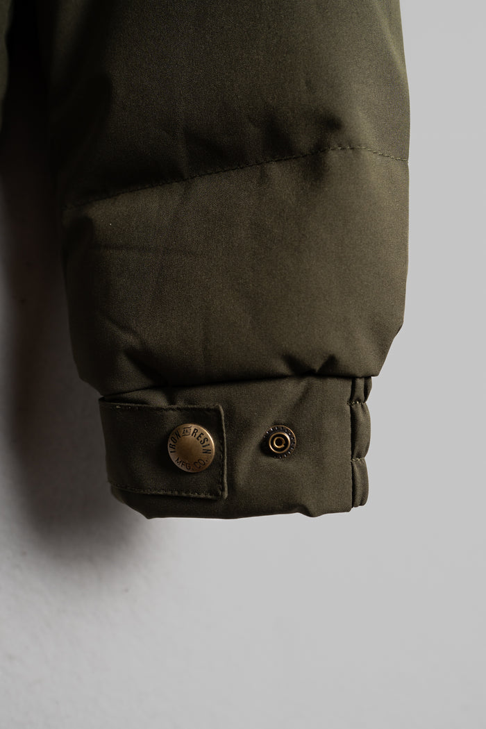 Close-up of a green jacket sleeve with a metal snap button labeled "Iron & Resin" against a neutral background.