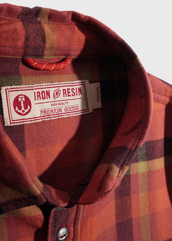 Close-up of a red plaid shirt collar with "Iron and Resin" label, showcasing high-quality premium goods.