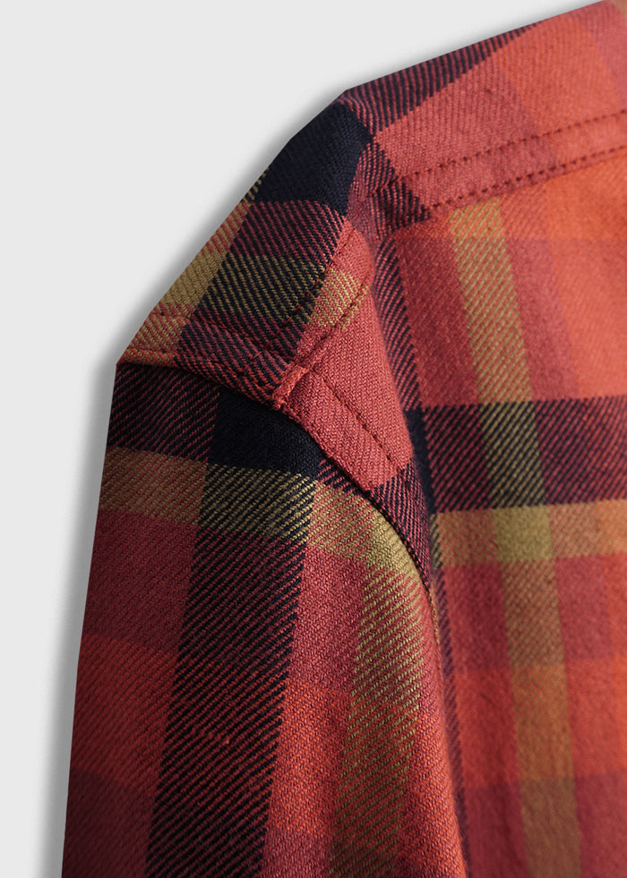 Close-up of a red plaid shirt shoulder, showcasing detailed stitching and vibrant pattern against a light gray background.