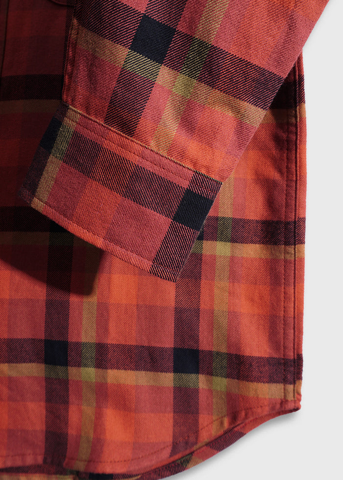 Close-up of a red plaid shirt sleeve with black and olive stripes, highlighting the cuff and fabric texture against a light background.