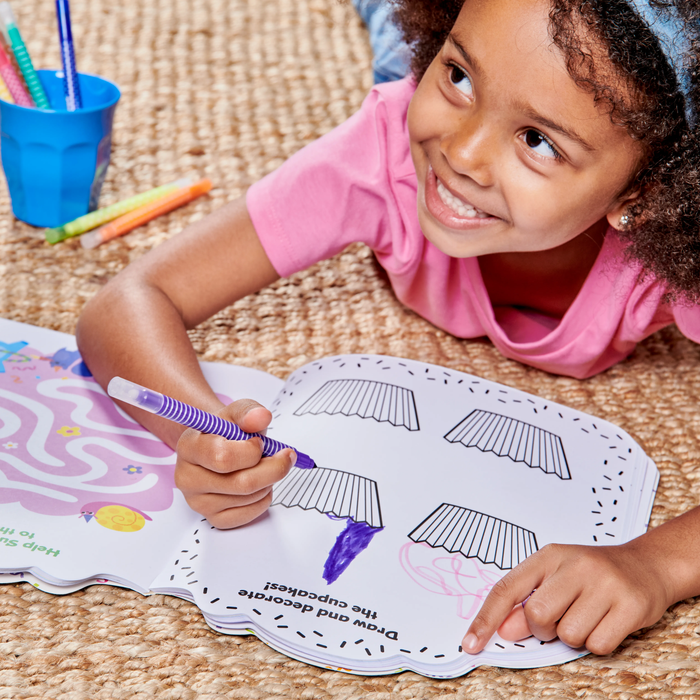Girl on floor drawing cupcakes in OOLY Playful Pages Activity Book - Games Coloring Stickers - Unicorn Party!