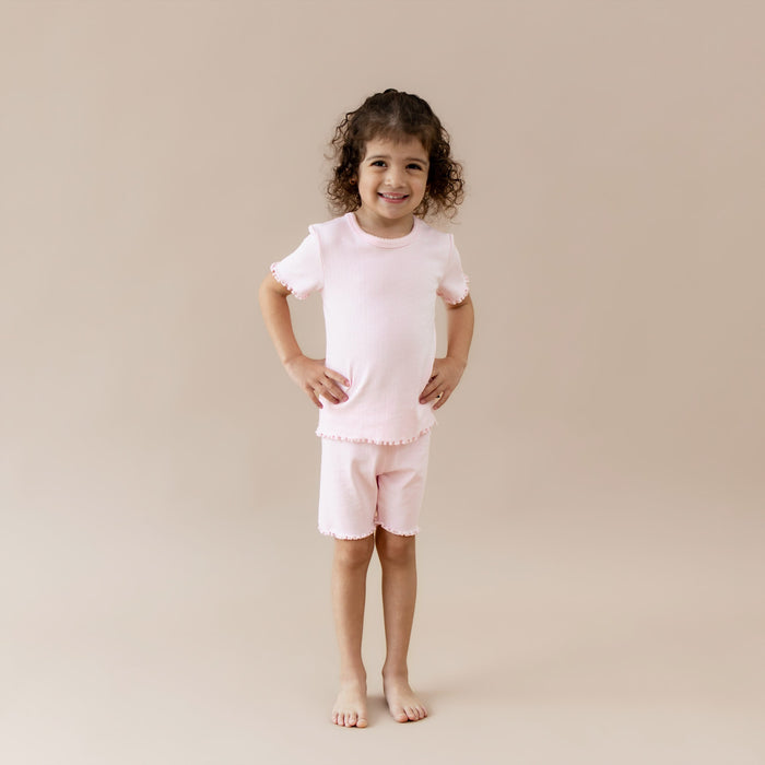 Child wearing a pink pointelle lounge outfit on a beige background