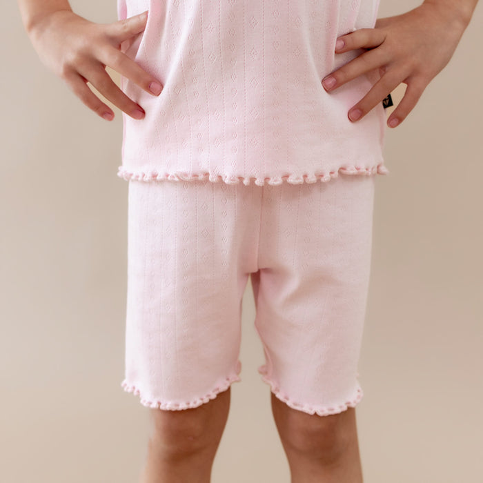 Person wearing a pink outfit with shorts and a top on a beige background