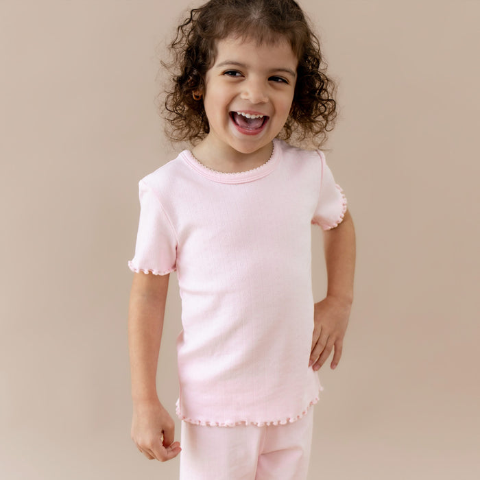 Child wearing a pink outfit with ruffled sleeves and hem on a beige background