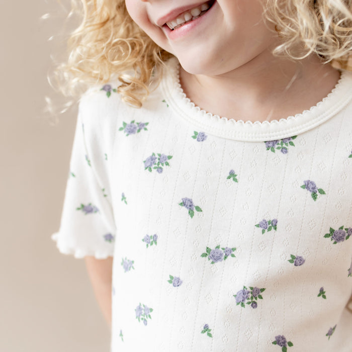 Child wearing a white shirt with purple floral patterns on a plain background