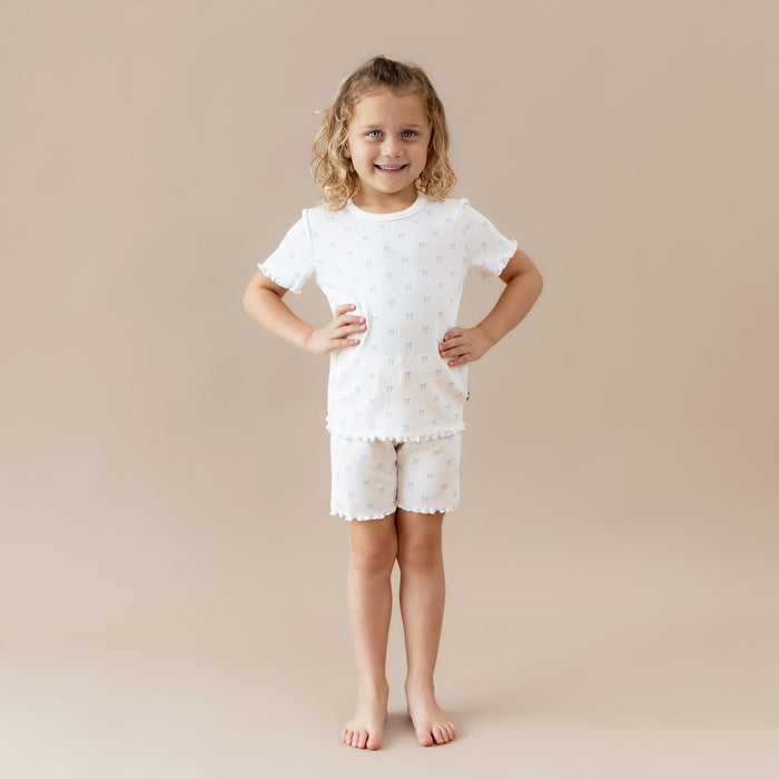 Young girl wearing a white pointelle outfit with blue bow pattern on a beige background