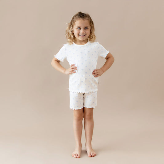Young girl wearing a white pointelle outfit with blue bow pattern on a beige background