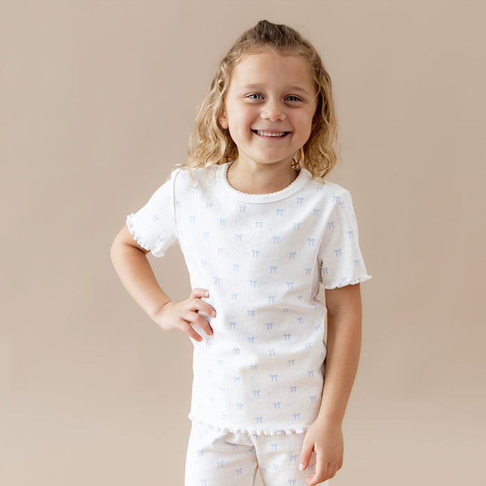 Young girl wearing a white t-shirt with small blue bow patterns on a beige background