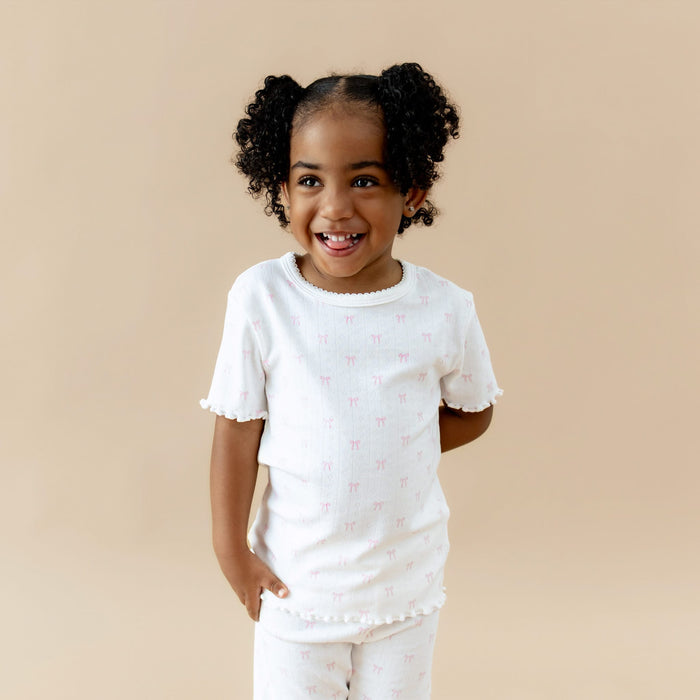 Child wearing a white t-shirt with a subtle pink bow pattern on a beige background