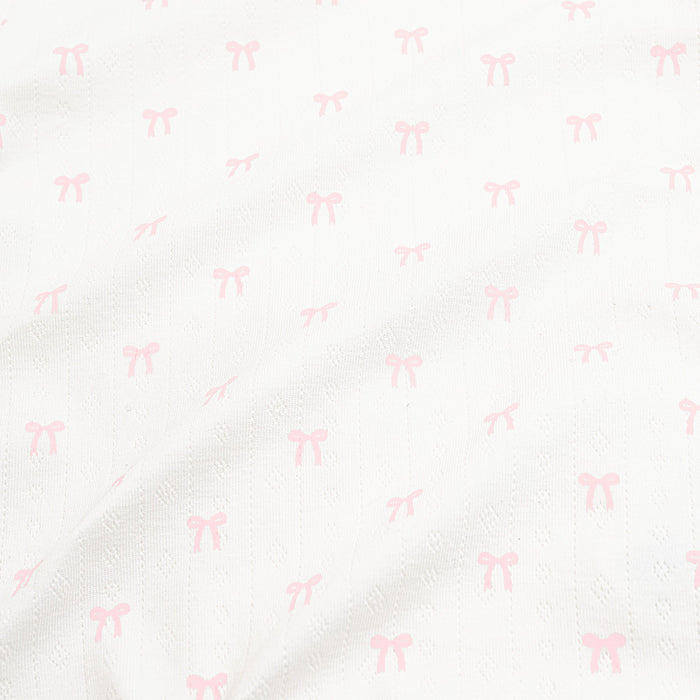 Close up of the pointelle fabric: An all-over print of dainty light pink bows over a white background.