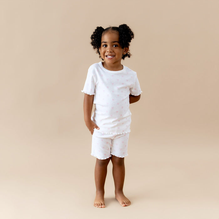 Young girl wearing a white outfit with pink bow print on a beige background