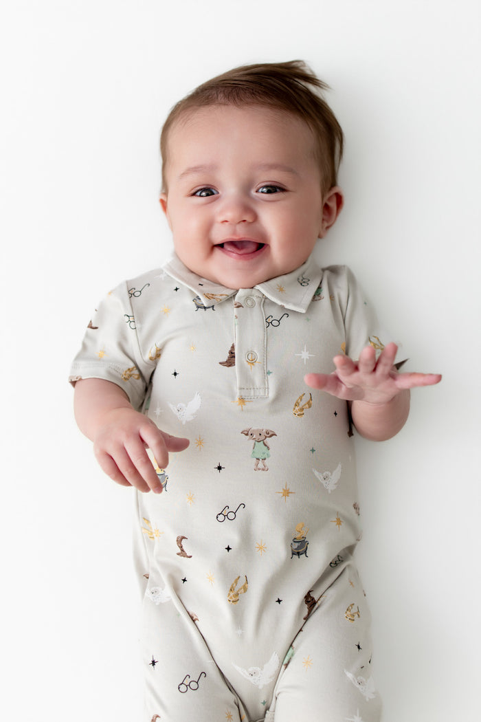 Baby wearing a cream polo shortall with Harry Potter prints on a white background