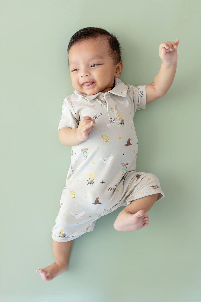 Baby wearing a Harry Potter patterned polo shortall on a green background