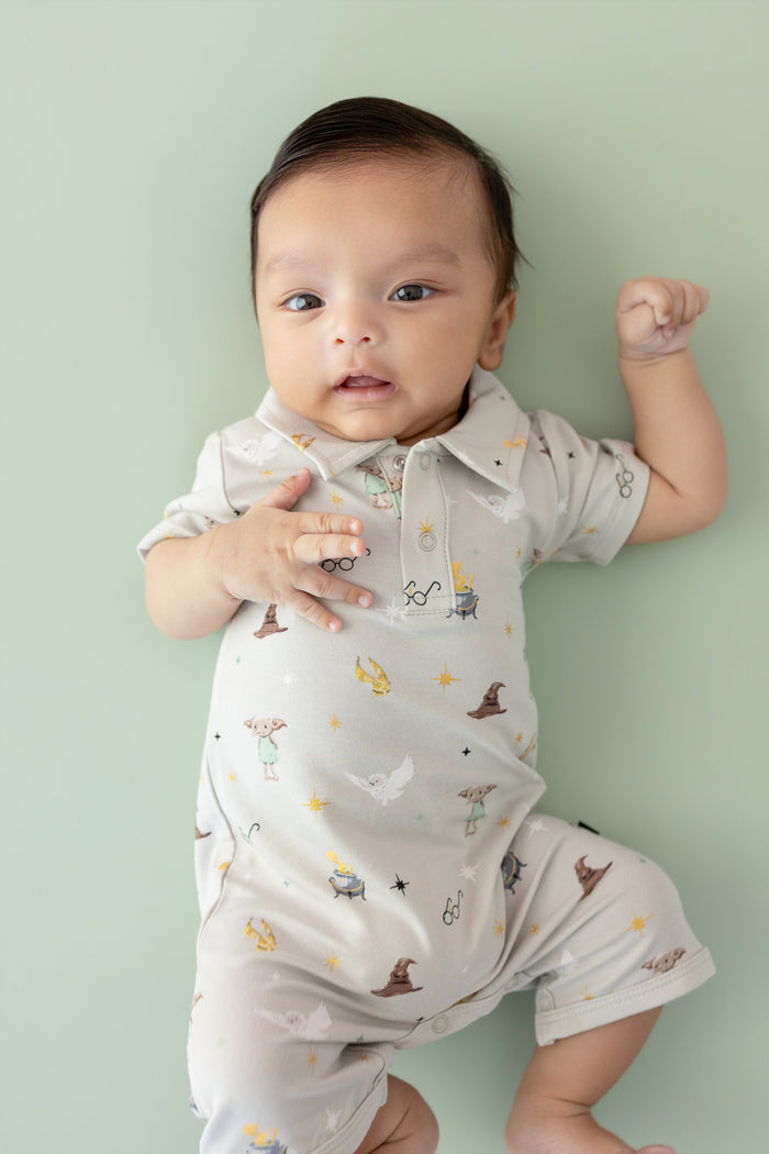 Baby wearing a cream polo shortall with Harry Potter prints on a green background