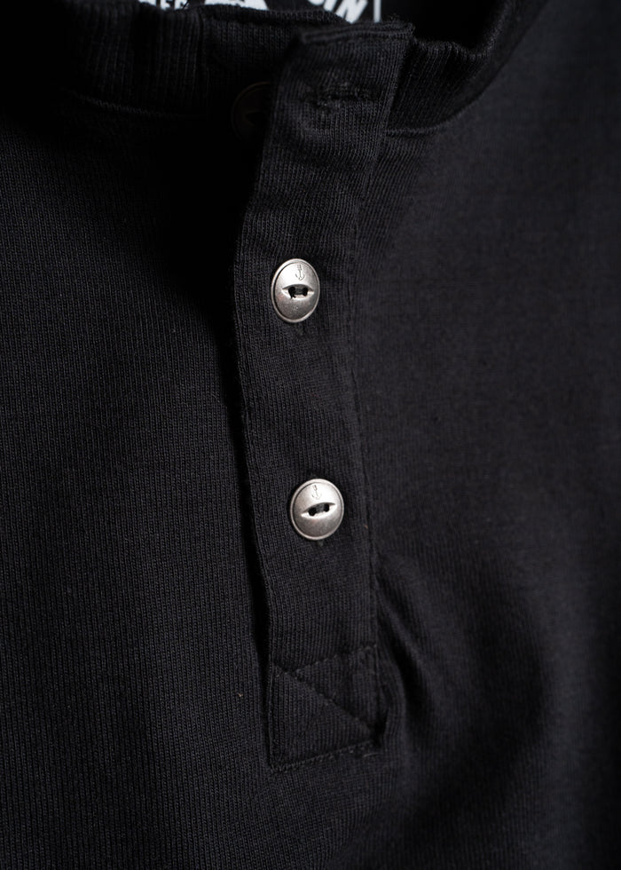Close-up of a black henley shirt with two metal buttons, highlighting the textured fabric and button details.