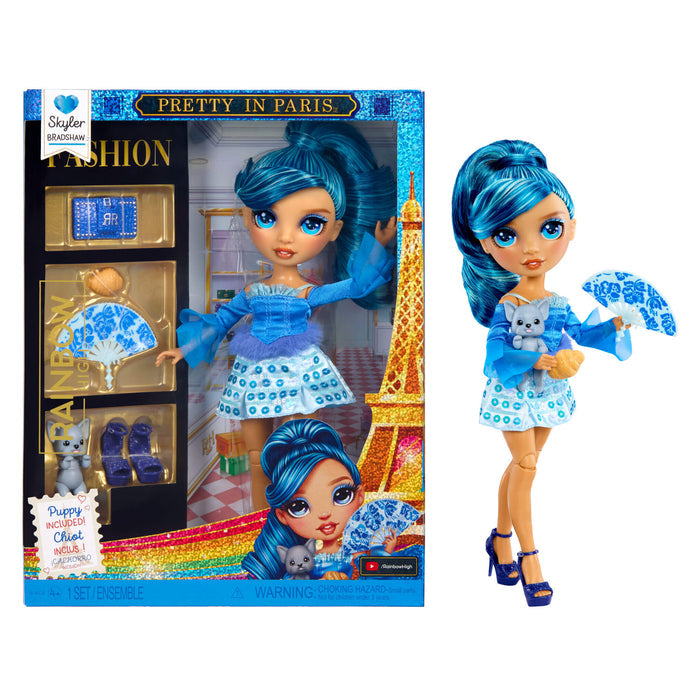 Fashion doll with blue hair and outfit, holding a puppy and a fan, next to its packaging