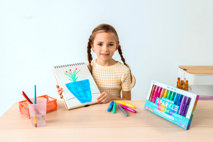 Girl holding completed coloring of blue flower pot with OOLY Rainbow Sparkle Metallic Watercolor Gel Crayons