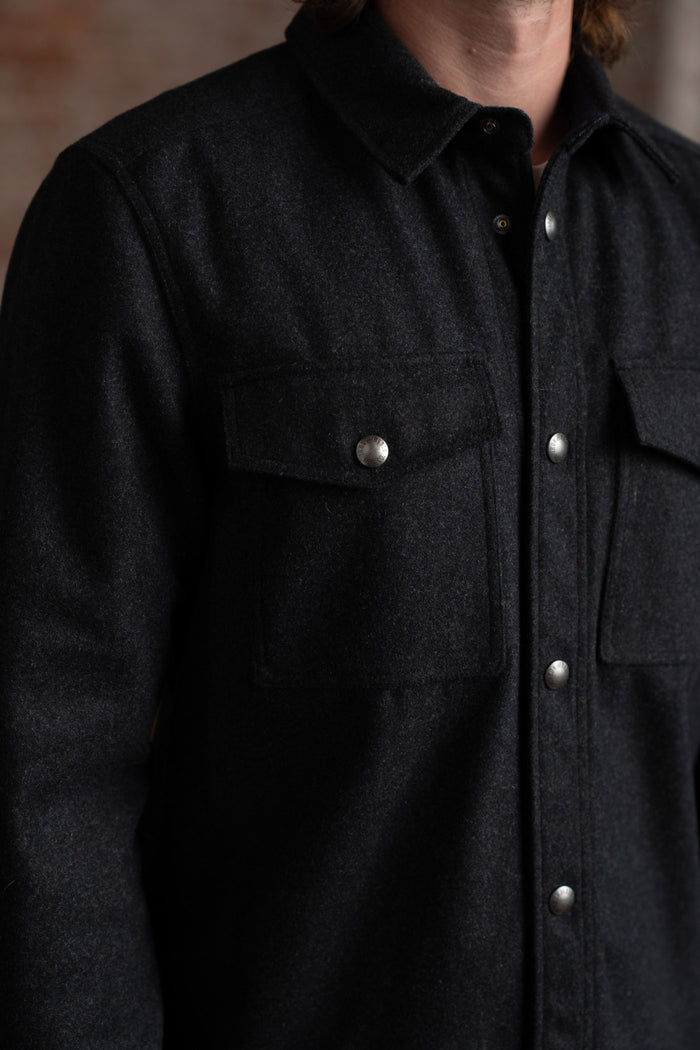 Close-up of a person wearing a dark wool shirt with metal buttons and chest pockets, highlighting the texture and design.