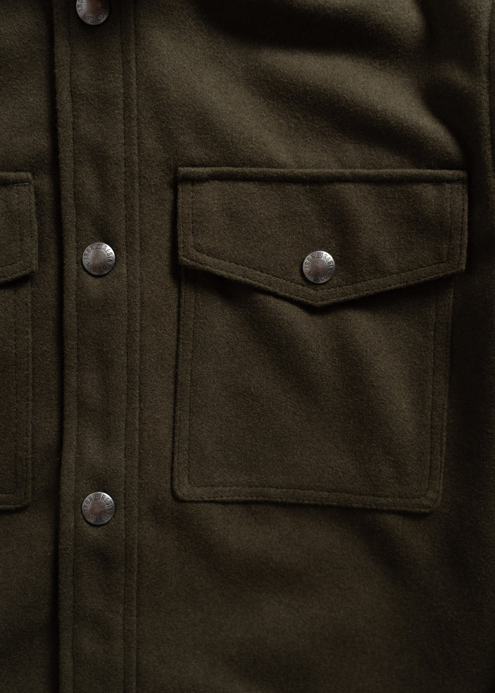 Close-up of an olive green wool jacket with metal snap buttons and two flap pockets, showcasing its rugged texture and design.