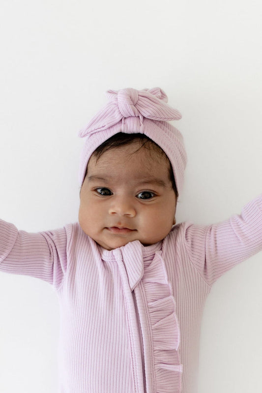 Infant wearing the Ribbed Headwrap in Thistle with matching ribbed ruffle zipper footie