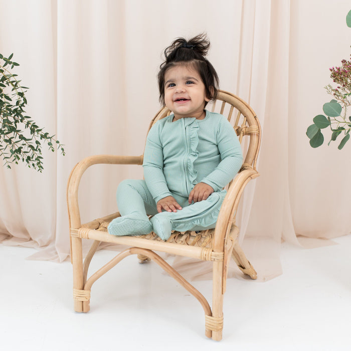Toddler wearing Kyte Baby Ribbed Ruffle Zipper Footie in Sage green