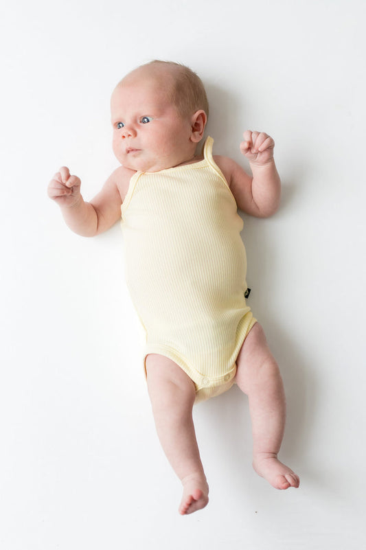 Newborn laying on a white surface wearing the Ribbed Spaghetti Strap Bodysuit in Chamomile