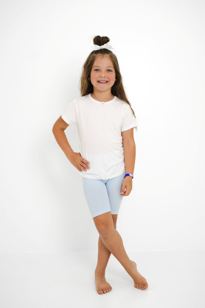 Young girl posing wearing the Ribbed Toddler Biker Shorts in Breeze paired with a white shirt