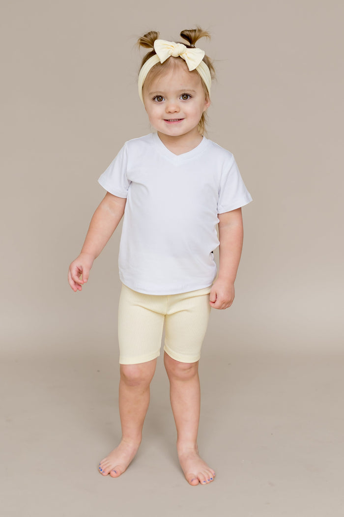 Young girl wearing the Ribbed Toddler Biker Shorts in Chamomile with a whitev-neck