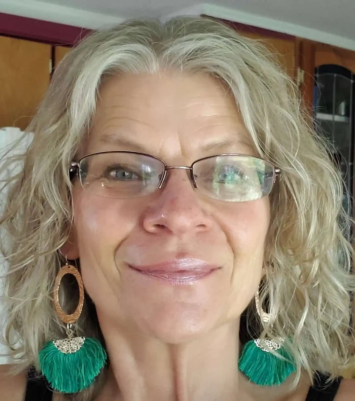 Rose Gold Filigree Silk Tassel Earrings Copper Embossed worn by a person with wavy gray hair and glasses.