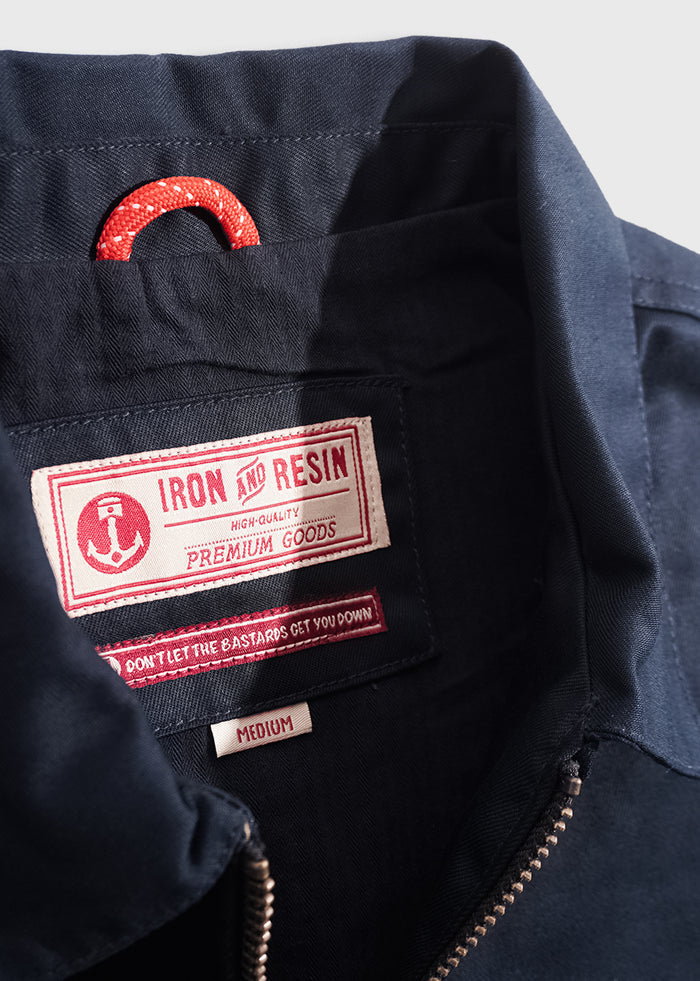 Close-up of a navy jacket's inner label showing "Iron and Resin" branding, size medium, and a red loop for hanging.