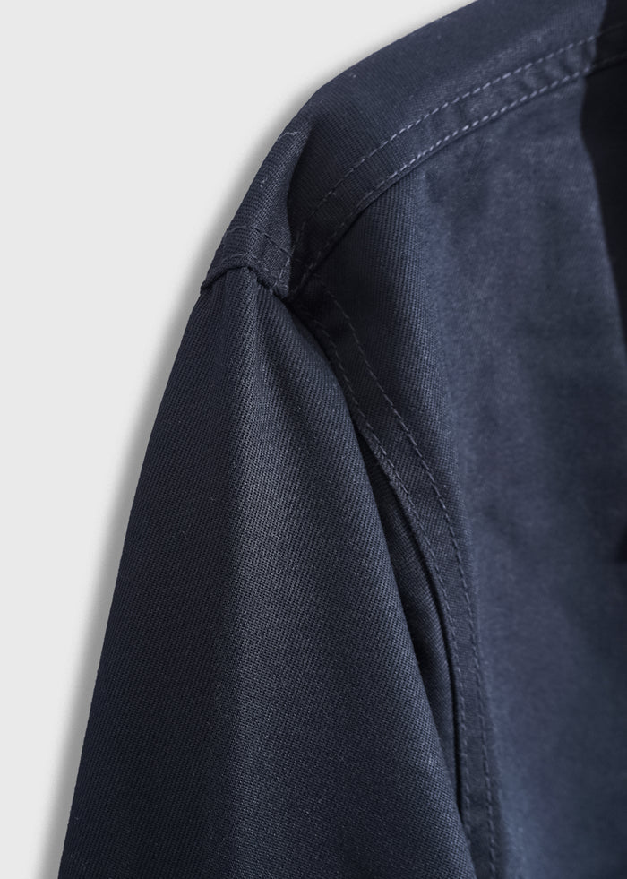 Close-up of a dark blue shirt's shoulder seam, highlighting the fabric texture and stitching detail against a light background.
