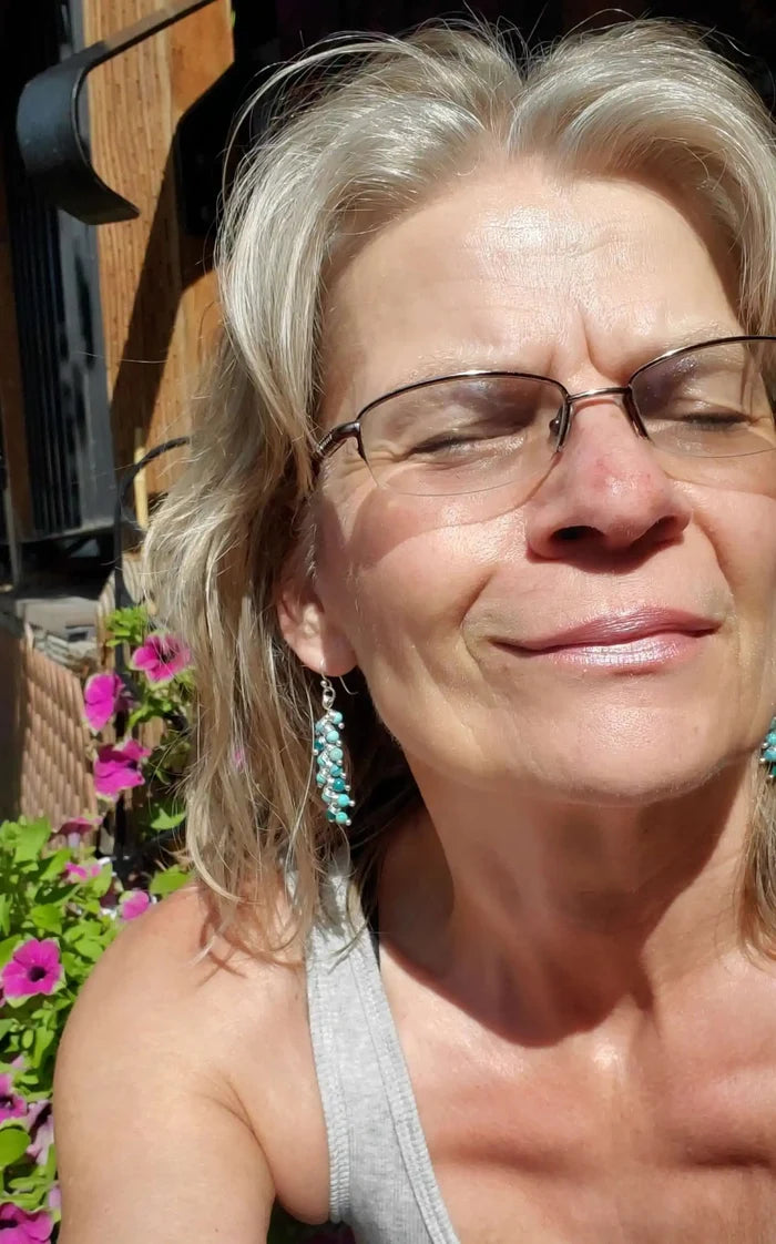 Woman wearing Seen On Jane The Virgin Silver Turquoise Wire Coil Earrings, smiling in sunlight with flowers in the background.