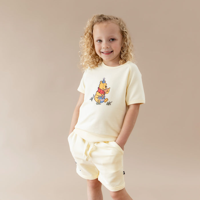 Young girl modeling the Short Sleeve Jogger Set in Winnie the Pooh on Chamomile with the hands in the pockets of the shorts