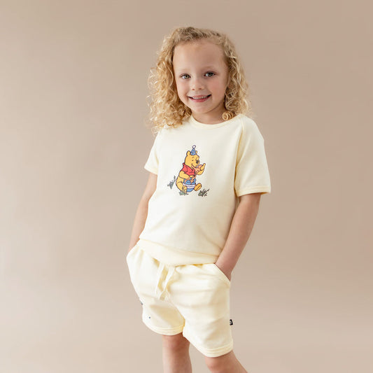 Young girl modeling the Short Sleeve Jogger Set in Winnie the Pooh on Chamomile with the hands in the pockets of the shorts