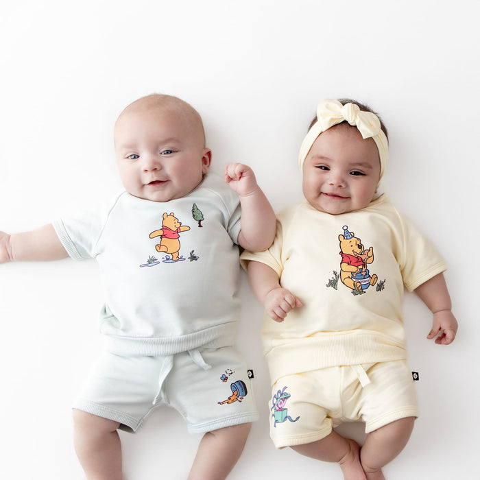 Two infants laying side by side wearing the Short Sleeve Jogger Set in Winnie the Pooh on Chamomile and Winnie the Pooh in Dew