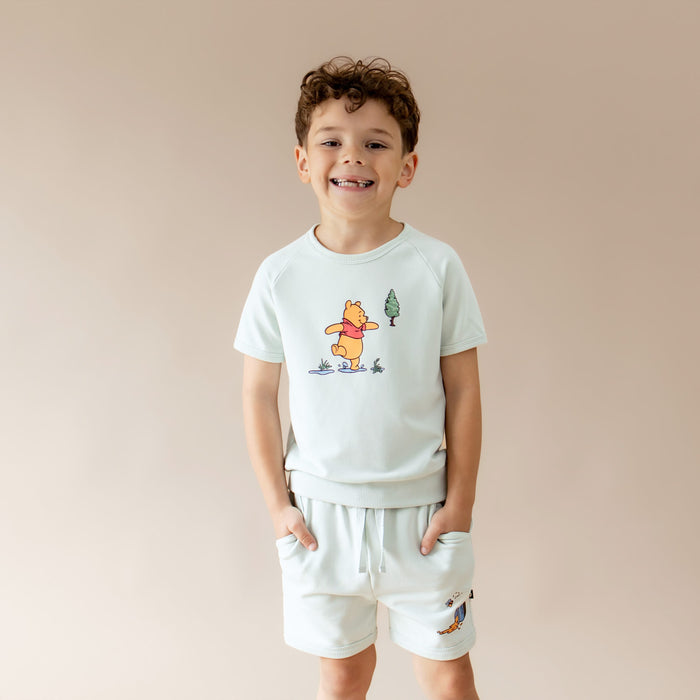 Young boy modeling the Short Sleeve Jogger Set in Winnie the Pooh on Dew with the hands in the shorts pockets