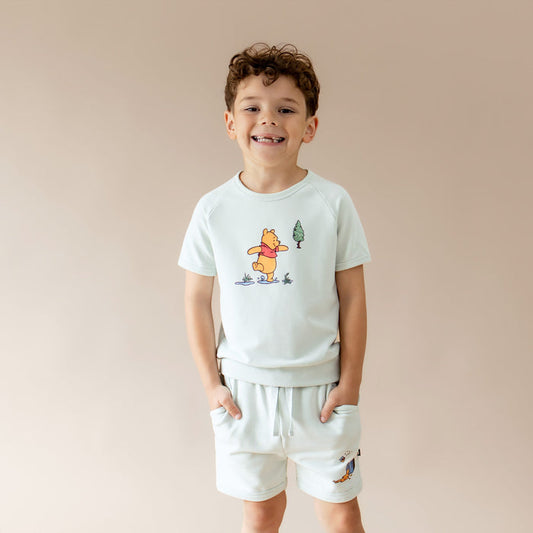Young boy modeling the Short Sleeve Jogger Set in Winnie the Pooh on Dew with the hands in the shorts pockets