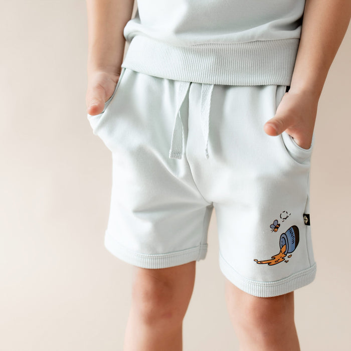 Close up of the single graphic of a honey pot on its side with honey spilling out on the shorts of the Short Sleeve Jogger Set in Winnie the Pooh on Dew