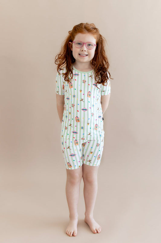 Child wearing a green and white striped short sleeve pajamas with colorful Harry Potter patterns on a beige background