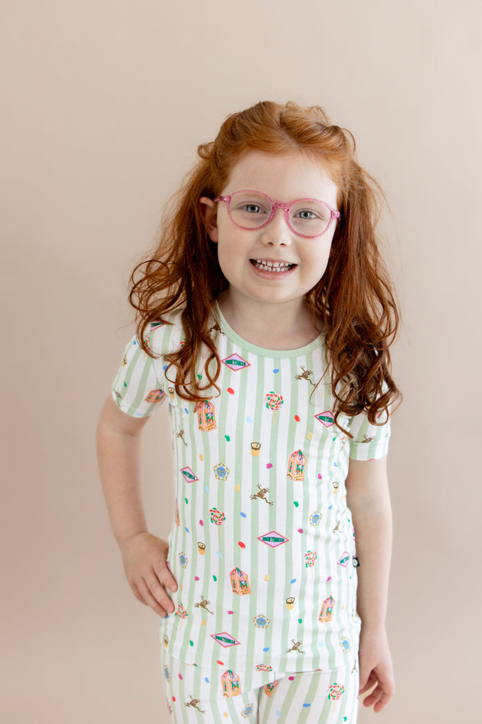Child wearing a green and white striped Short Sleeve Pajamas with colorful Harry Potter patterns on a beige background
