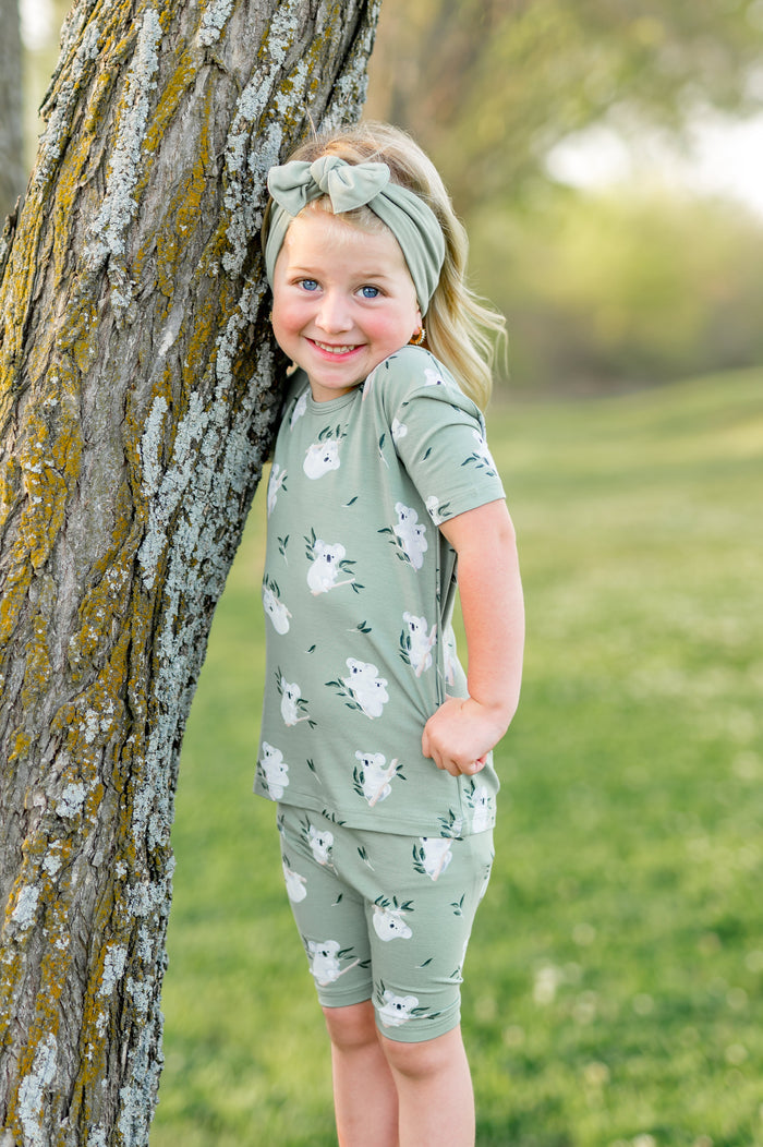 Young girl posing against a tree wearing the Short Sleeve Pajamas in Koala