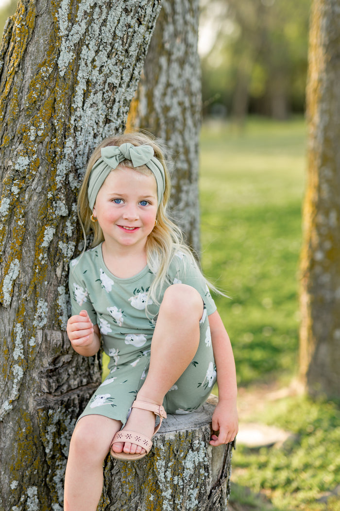 Young girl sitting on a tree stump beside a tree wearing the Short Sleeve Pajamas in Koala